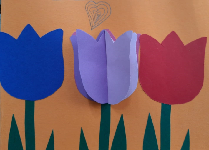 Eine selbst gebastelte Karte mit einer blauen, einen lilanen und einer roten Tulpe und einem mit Bleistift gezeichnetem Herz